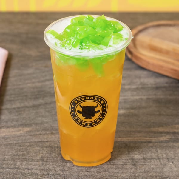 A SNO CREAM COMPANY drink with orange liquid and green jelly toppings on a wooden table.