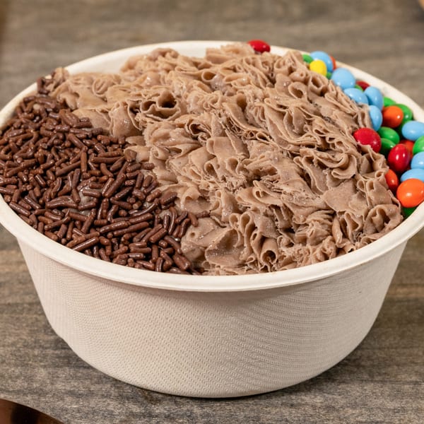 Shaved chocolate ice dessert with chocolate sprinkles and colorful candies in a white bowl.