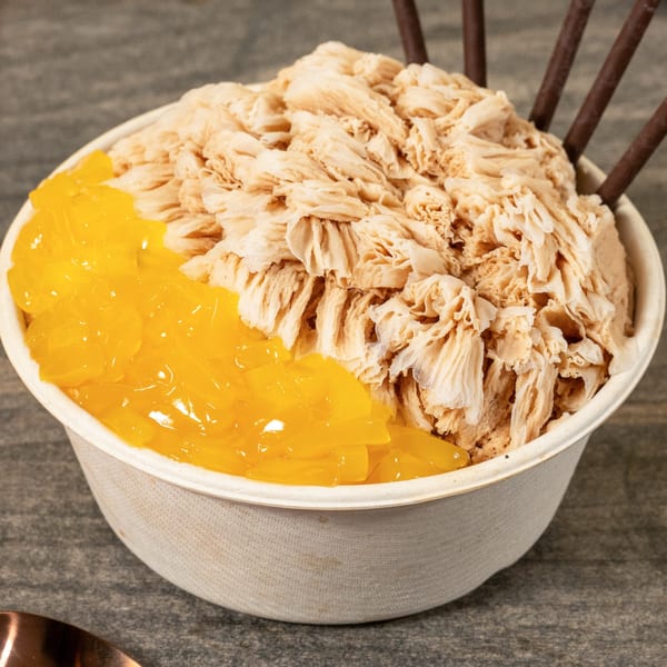 A bowl of shaved ice dessert with brown sugar flavor and bright yellow mango jelly.
