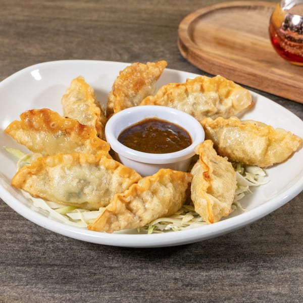 Golden-fried Asian dumplings with a side of dark dipping sauce, served on shredded cabbage.